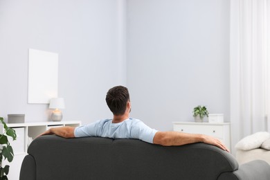 Photo of Happy man resting on sofa at home, back view