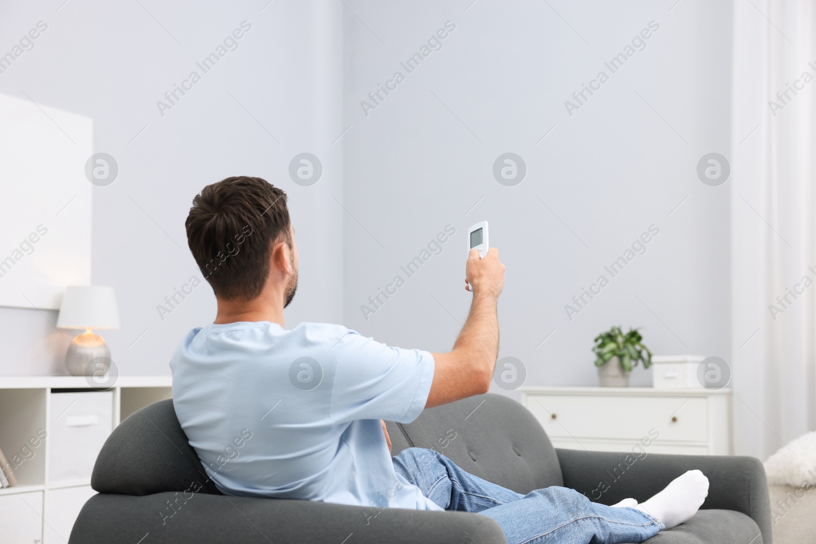 Man using remote to control air conditioner on sofa at home. Space for text Photo of Man using remote to control air conditioner on sofa at home. Space for text