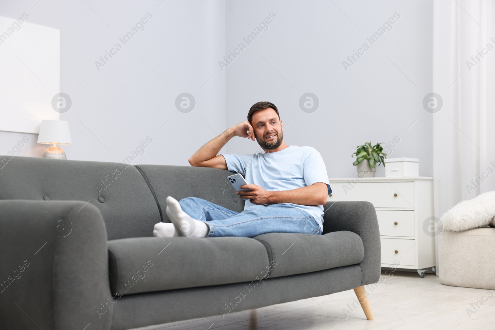 Photo of Man with smartphone on sofa at home