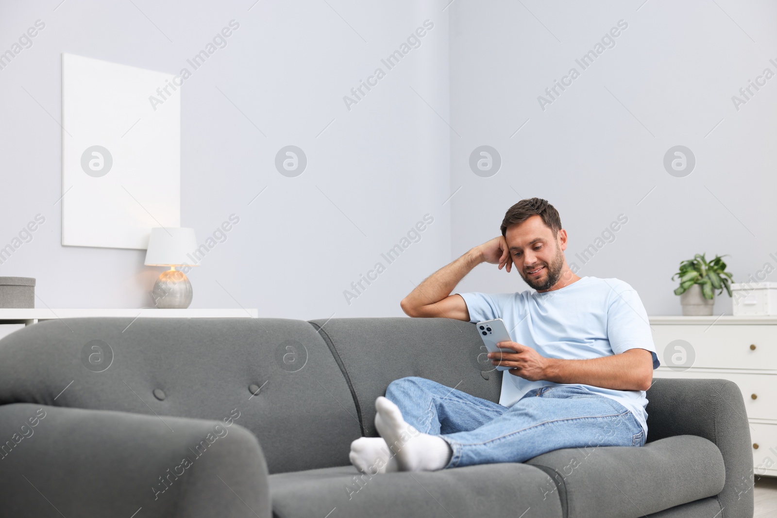 Man with smartphone on sofa at home. Space for text Photo of Man with smartphone on sofa at home. Space for text