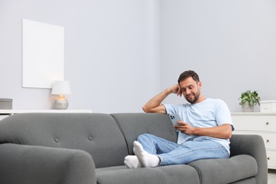 Photo of Man with smartphone on sofa at home. Space for text
