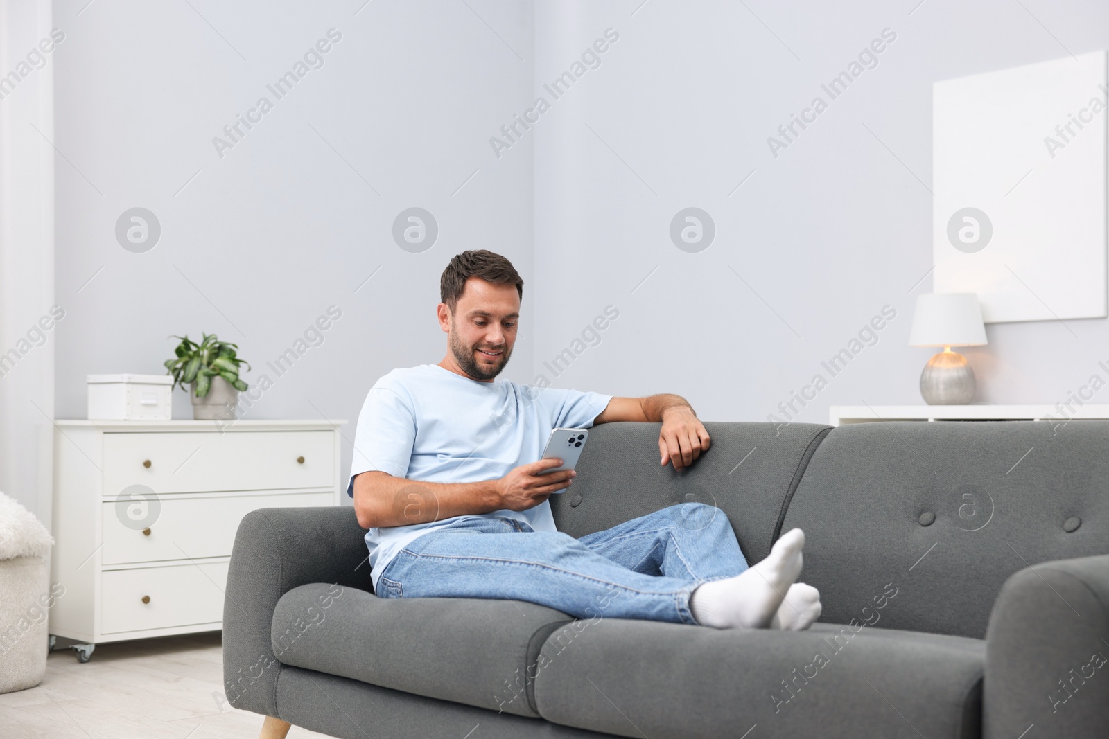 Photo of Man with smartphone on sofa at home