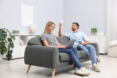 Photo of Couple with laptop and smartphone using remote to control air conditioner on sofa at home