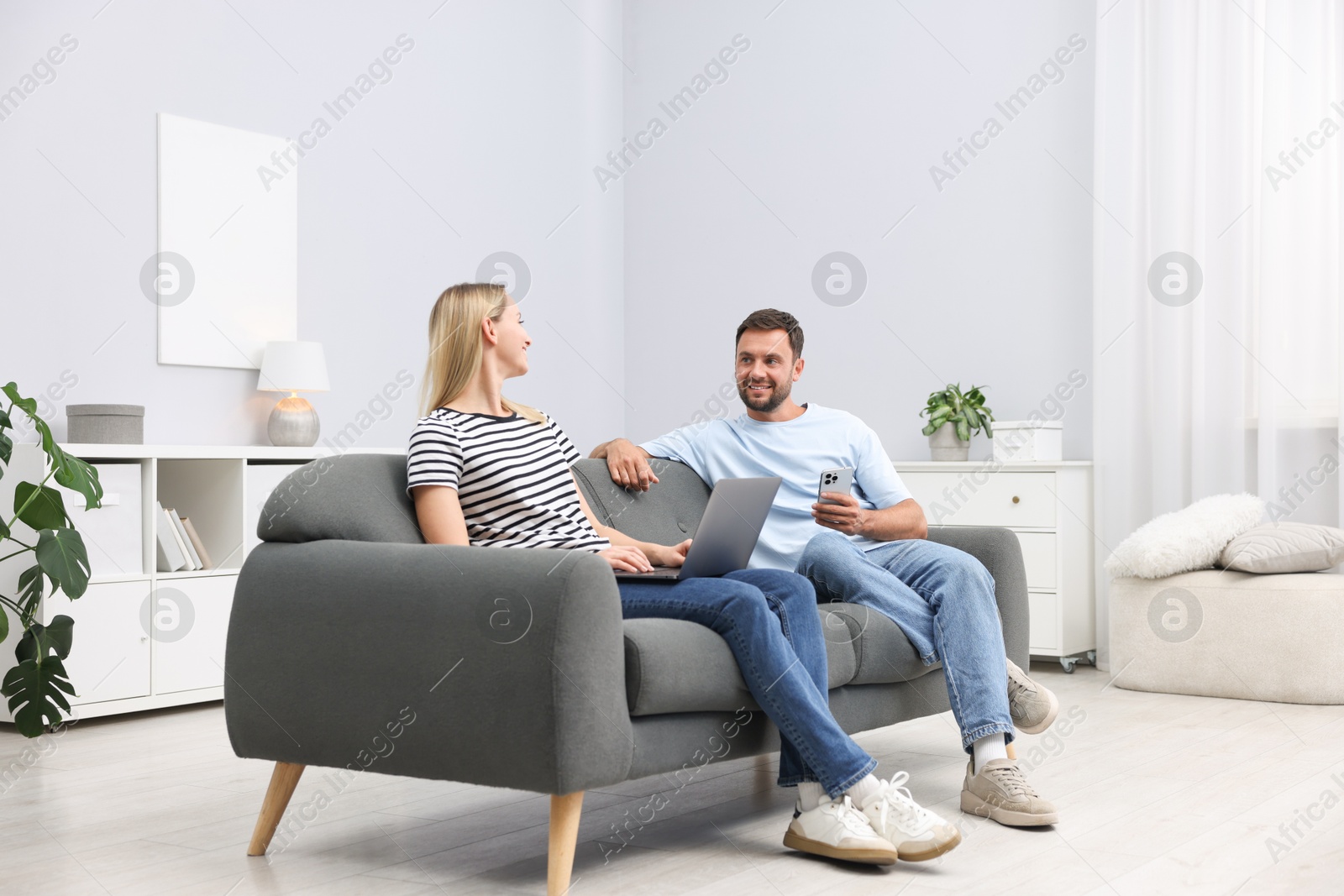 Photo of Happy couple with devices spending time together on sofa at home