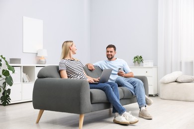 Photo of Happy couple with devices spending time together on sofa at home