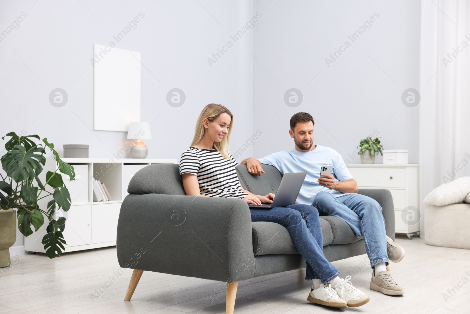 Photo of Happy couple with devices spending time together on sofa at home