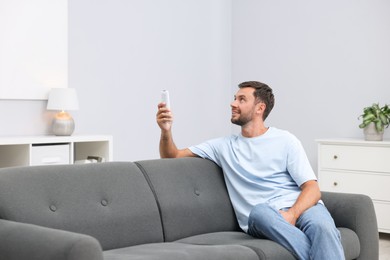 Photo of Man using remote to control air conditioner on sofa at home. Space for text
