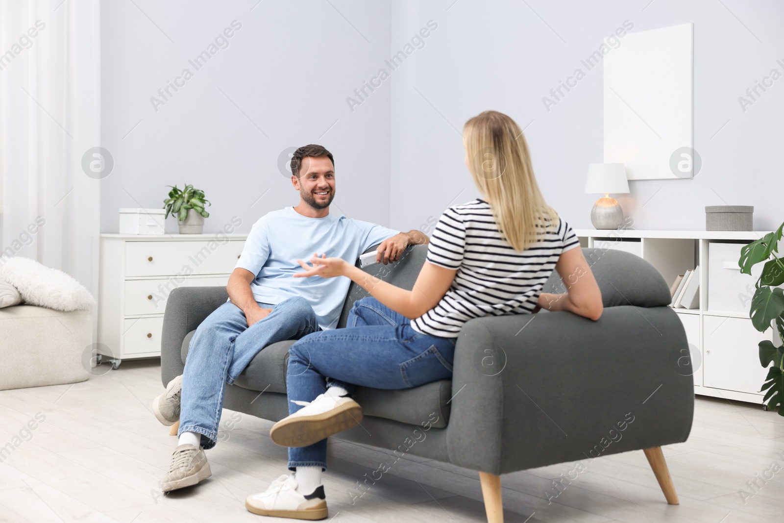 Photo of Couple with air conditioner remote control on sofa at home