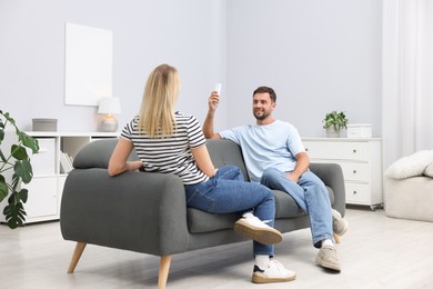 Photo of Couple using remote to control air conditioner on sofa at home