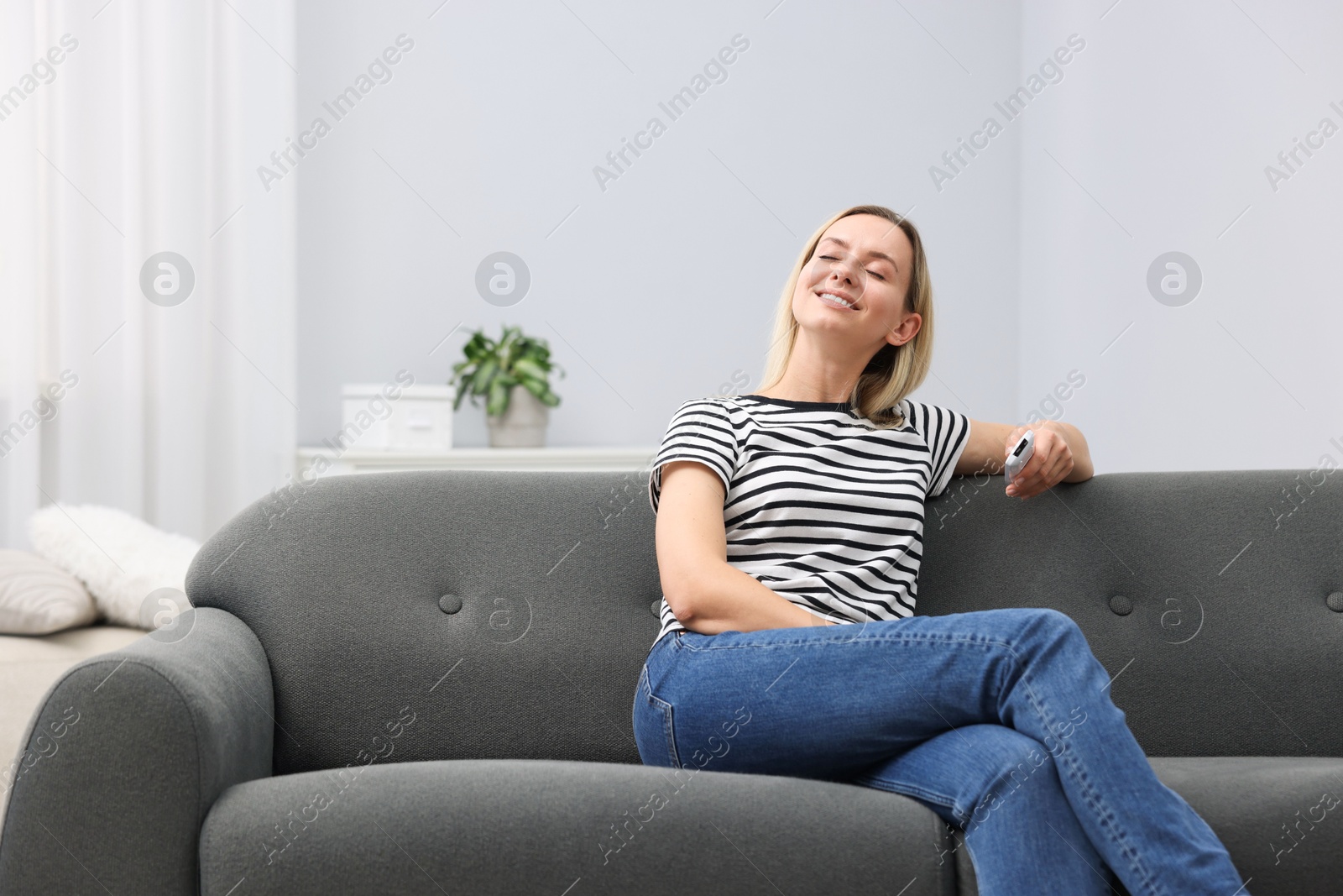 Photo of Woman with air conditioner remote control on sofa at home. Space for text
