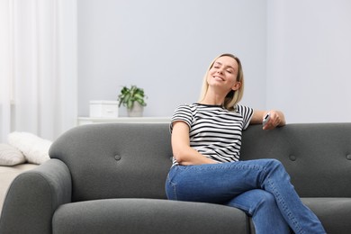 Photo of Woman with air conditioner remote control on sofa at home. Space for text