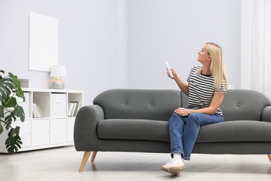 Photo of Woman using remote to control air conditioner on sofa at home. Space for text