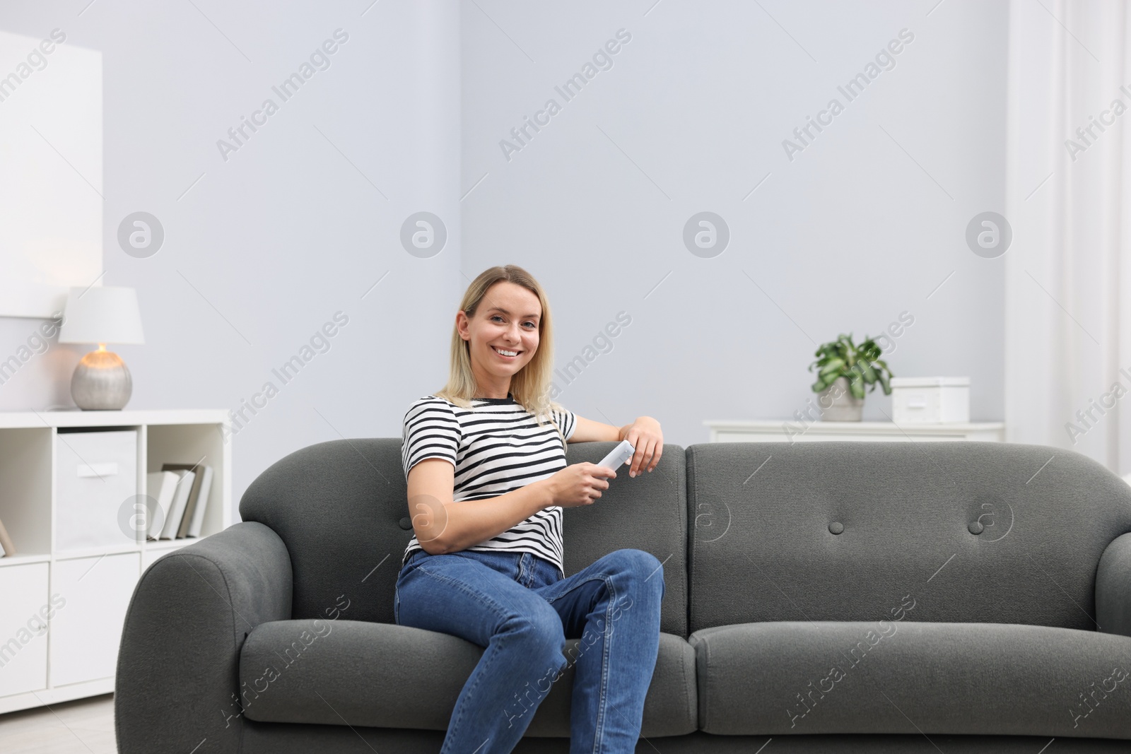 Photo of Woman with air conditioner remote control on sofa at home. Space for text
