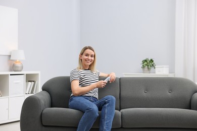 Photo of Woman with air conditioner remote control on sofa at home. Space for text