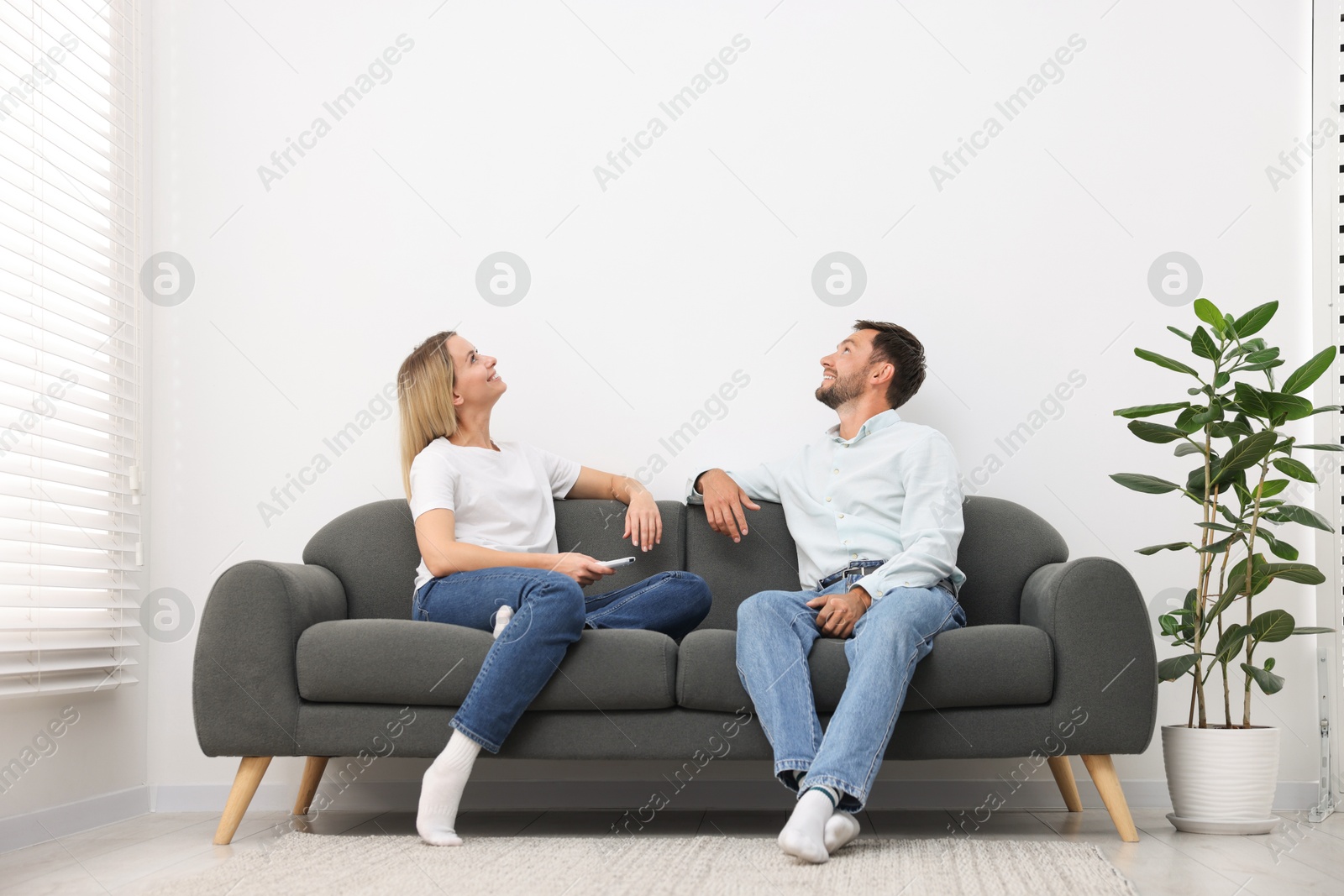 Photo of Couple using remote to control air conditioner on sofa at home