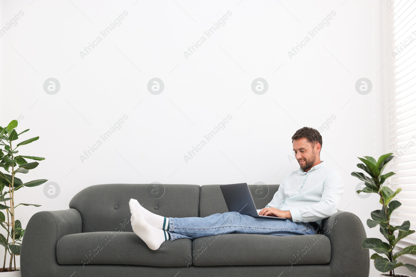Photo of Man with laptop on sofa at home. Space for text