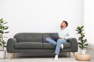 Photo of Man with laptop on sofa at home. Space for text