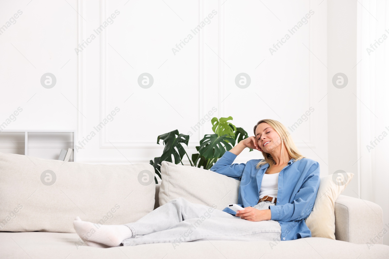 Photo of Woman with air conditioner remote control on sofa at home. Space for text