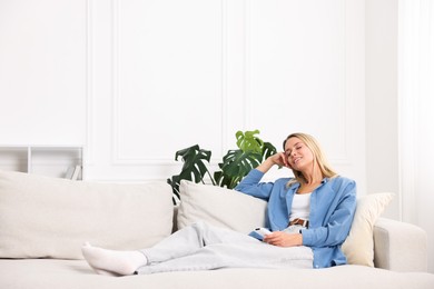 Photo of Woman with air conditioner remote control on sofa at home. Space for text