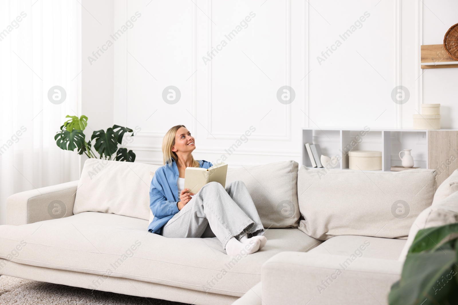 Photo of Woman reading book on sofa at home. Space for text