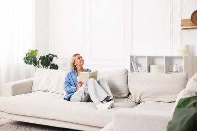 Photo of Woman reading book on sofa at home. Space for text