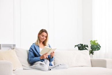 Photo of Woman reading book on sofa at home. Space for text