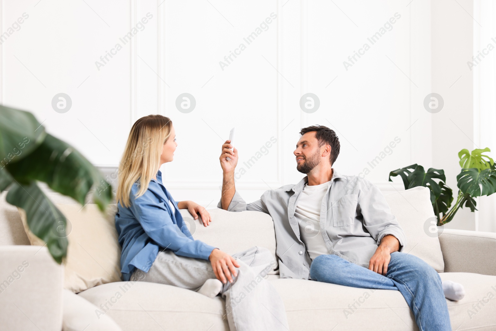 Photo of Couple using remote to control air conditioner on sofa at home
