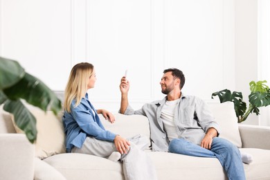 Photo of Couple using remote to control air conditioner on sofa at home