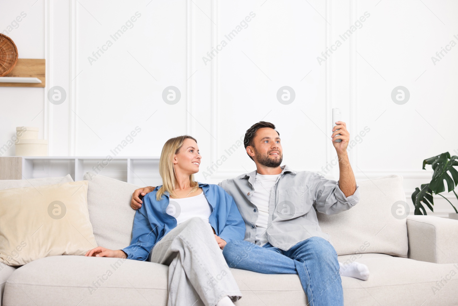 Photo of Couple using remote to control air conditioner on sofa at home