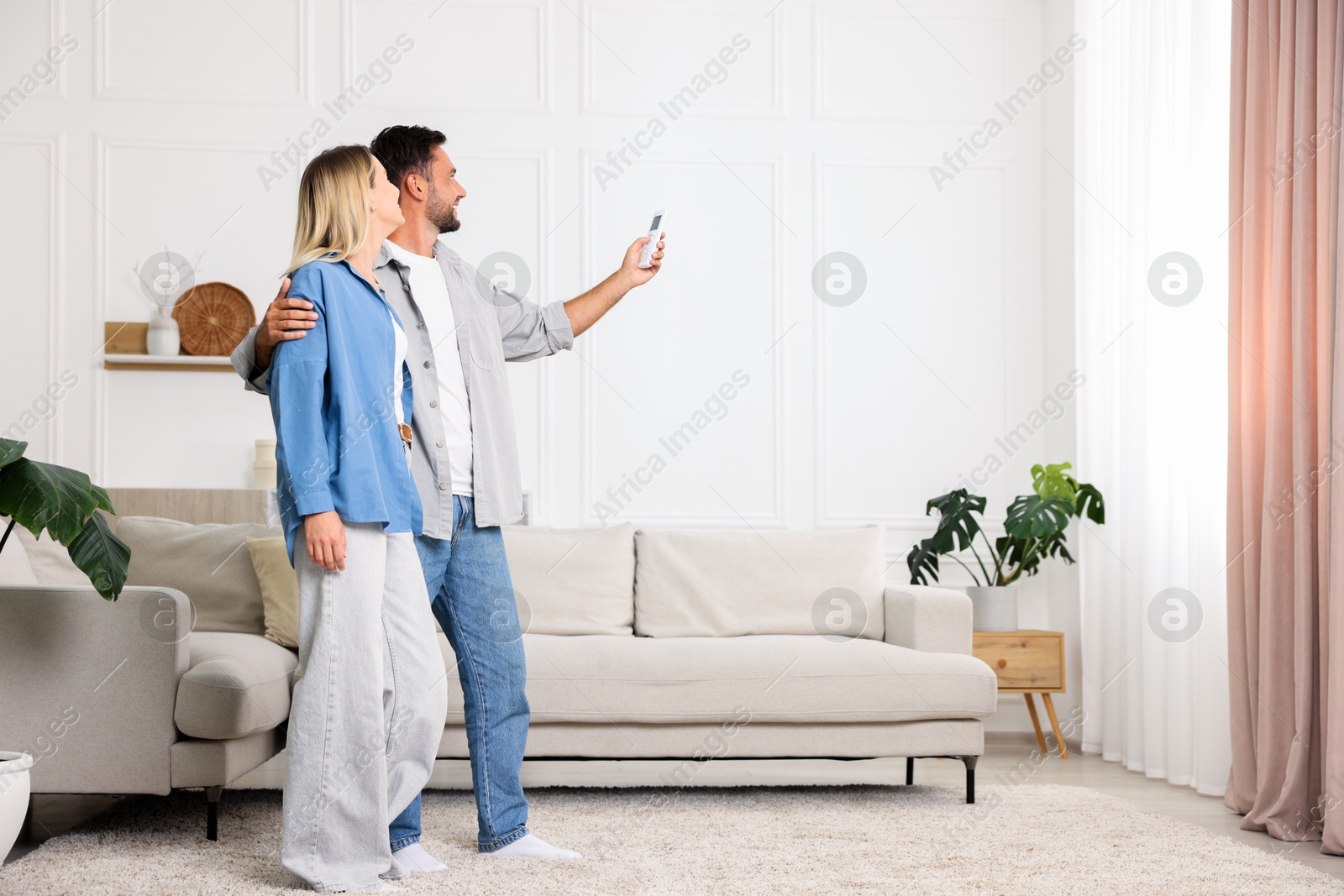 Photo of Couple using remote to control air conditioner at home. Space for text