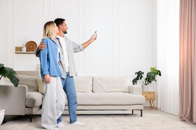 Photo of Couple using remote to control air conditioner at home. Space for text