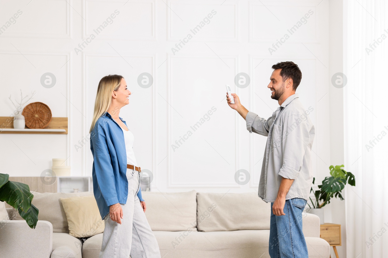 Photo of Couple using remote to control air conditioner at home