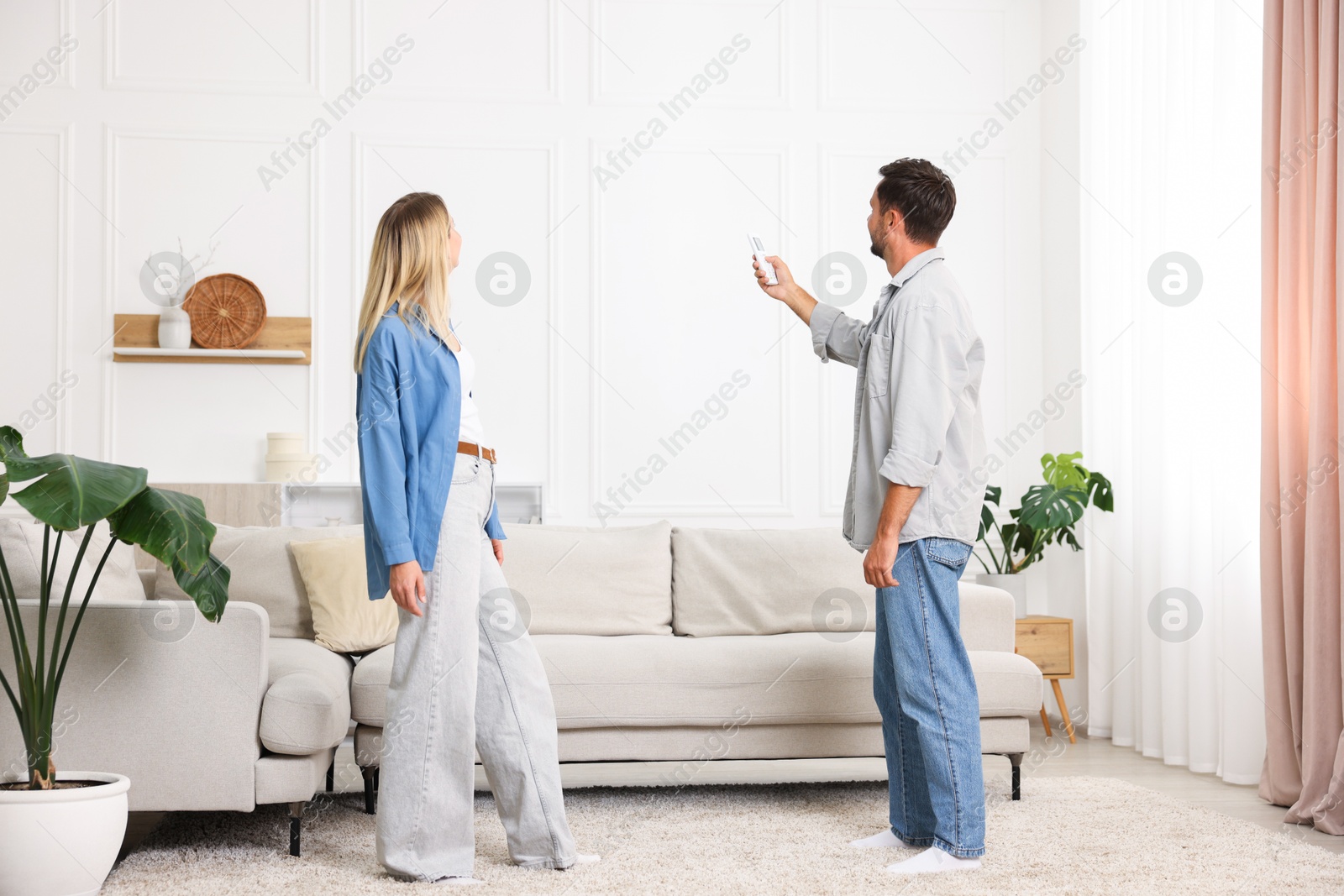 Photo of Couple using remote to control air conditioner at home