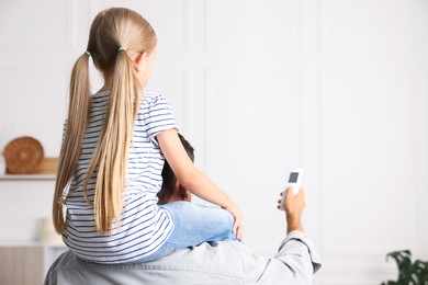 Photo of Father and daughter using remote to control air conditioner at home, back view. Space for text