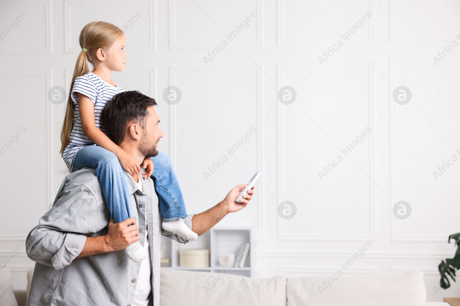 Photo of Father and daughter using remote to control air conditioner at home. Space for text