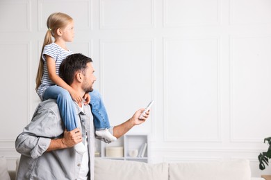 Photo of Father and daughter using remote to control air conditioner at home. Space for text