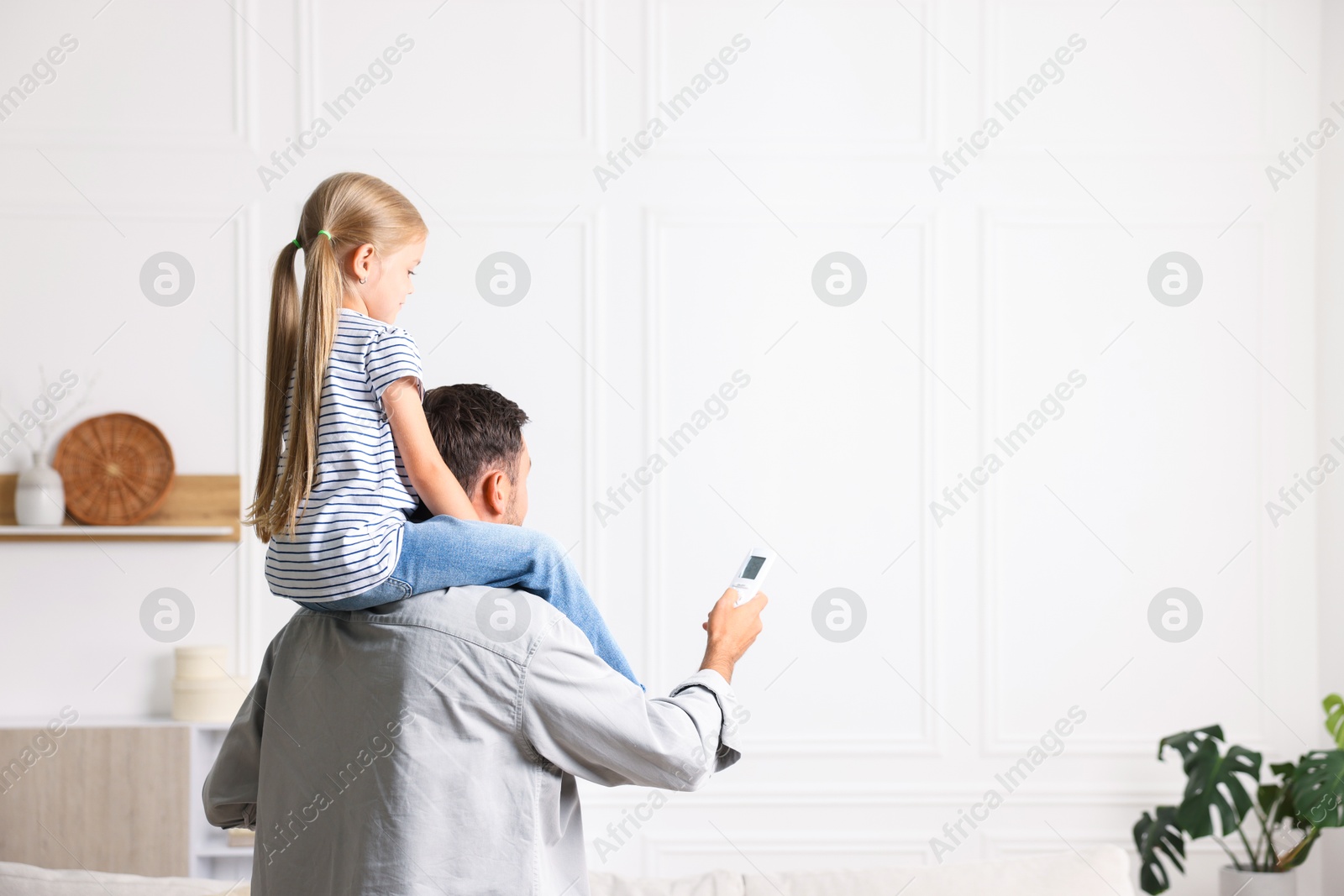Photo of Father and daughter using remote to control air conditioner at home. Space for text