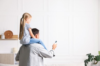 Photo of Father and daughter using remote to control air conditioner at home. Space for text