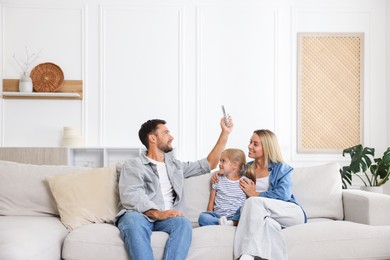 Photo of Happy family using remote to control air conditioner on sofa at home