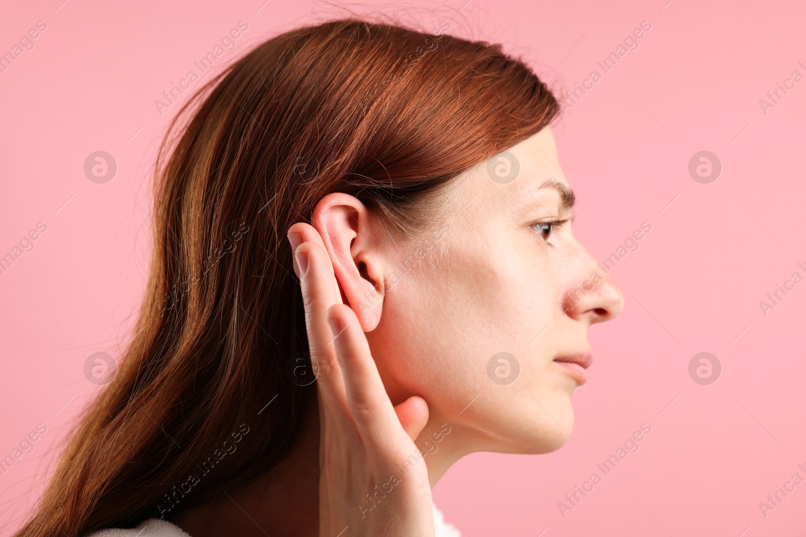 Photo of Sound. Woman showing hand to ear gesture on pink background