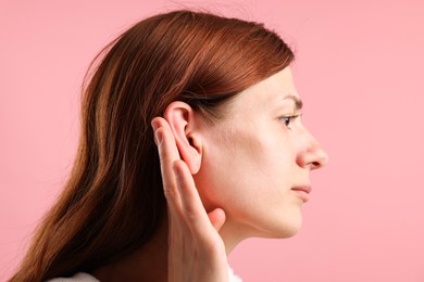 Photo of Sound. Woman showing hand to ear gesture on pink background
