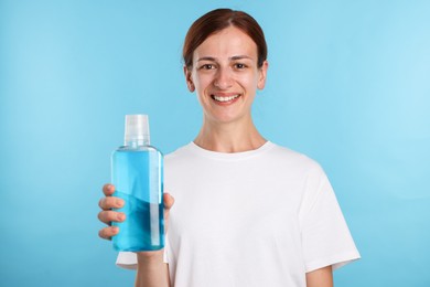 Photo of Woman rinsing mouth with mouthwash on light blue background