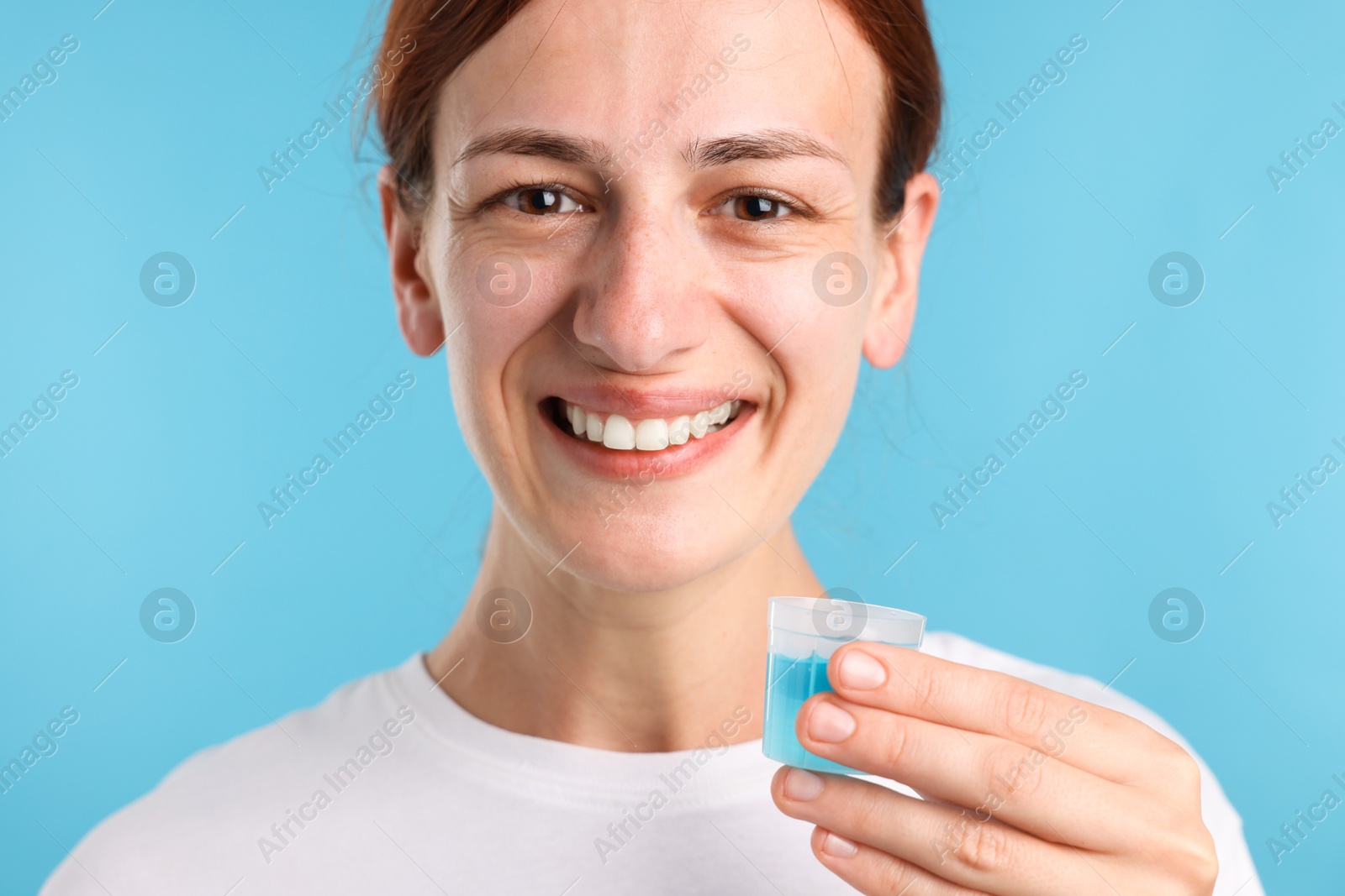 Photo of Woman rinsing mouth with mouthwash on light blue background