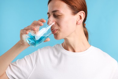 Photo of Woman rinsing mouth with mouthwash on light blue background