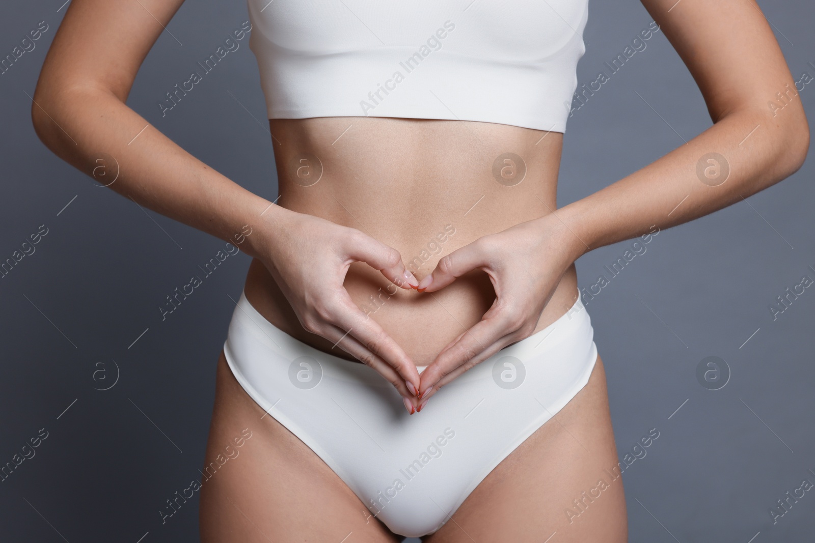 Photo of Young woman with flat belly making heart gesture on grey background, closeup