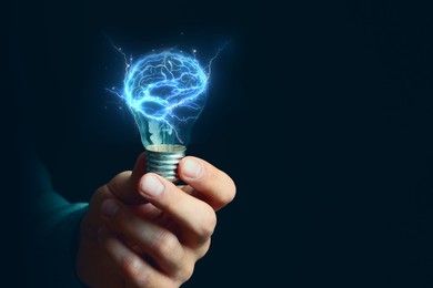 Image of Man holding light bulb with brain illustration inside against dark background, closeup. Idea concept