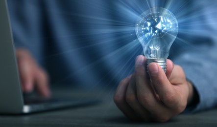 Image of Man holding light bulb with brain illustration inside at table, closeup. Idea concept