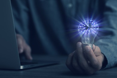 Image of Man holding light bulb with brain illustration inside at table, closeup. Idea concept
