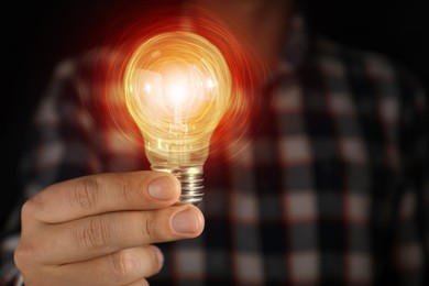 Image of Man holding glowing light bulb in darkness, closeup. Idea concept