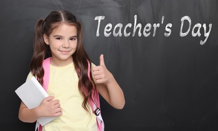 Image of Happy Teacher's Day. Cute little girl showing thumbs-up near blackboard